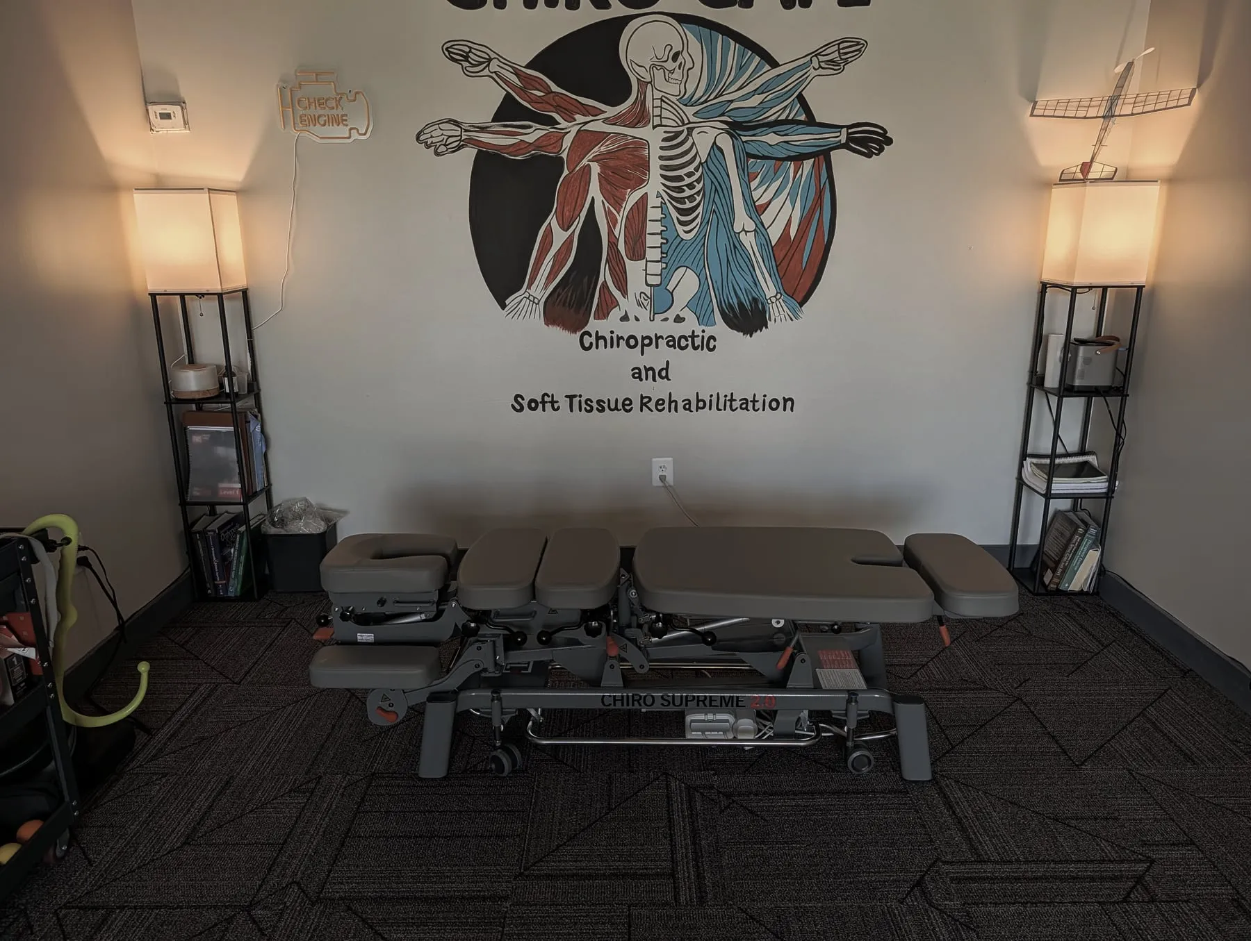 The Chiro Cafe treatment room inside CrossFit Garage: a hand-painted logo mural on the wall, a neon check-engine-light sign, and a model aeroplane on the shelf — the three details this page's argument is built on.