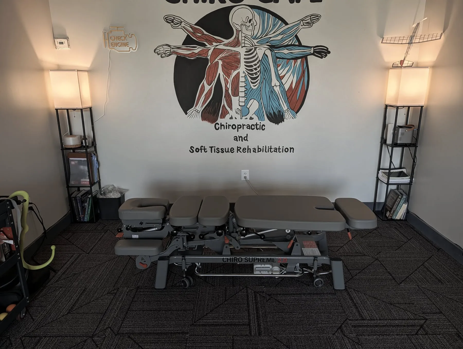 The Chiro Cafe treatment room inside CrossFit Garage: a hand-painted logo mural on the wall, a neon check-engine-light sign, and a model aeroplane on the shelf — the three details this page's argument is built on.